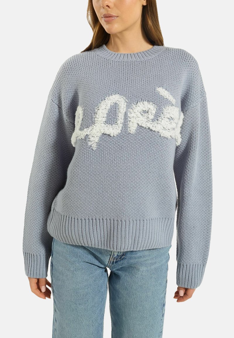 Light blue knitted sweater with a textured, fluffy white "hope" design across the front; ribbed cuffs and hem. Paired with blue jeans.
