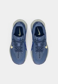Blå sportskor med ett ventilerande mesh-övre, texturerade overlay, kontrasterande mörkblå snören och en gyllen Nike-logga.