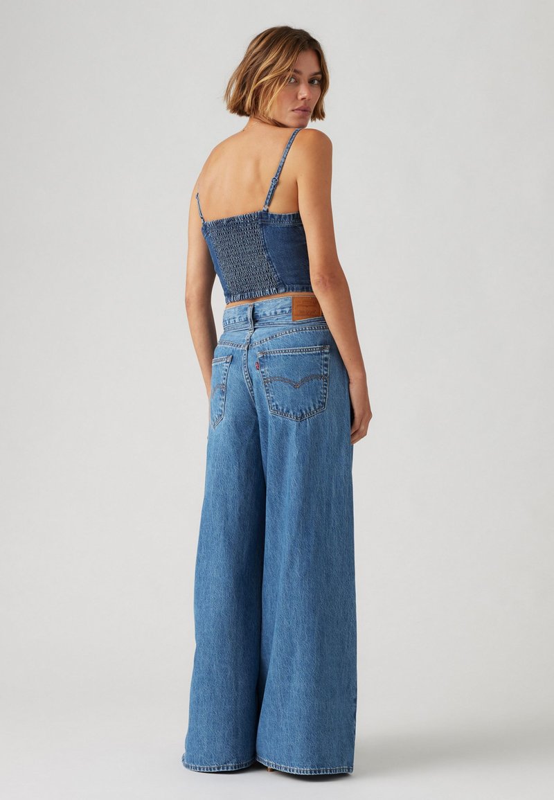 Un jean en denim bleu à jambes larges associé à un crop top ajusté à smocks. Détails remarquables incluent une taille haute et des poches arrière.