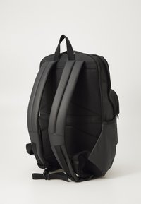Sac à dos noir avec un tissu rembourré, un design épuré, un panneau arrière en maille, des bretelles épaisses réglables et une poche latérale pour les accessoires.