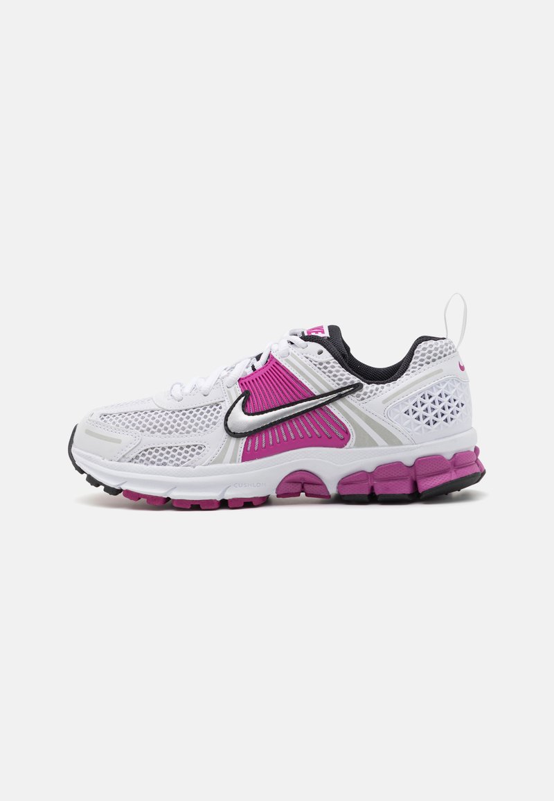 Baskets de sport blanches avec des accents roses, tige en mesh, semelle rembourrée, détails noirs et un logo Nike réfléchissant en argent sur le côté.