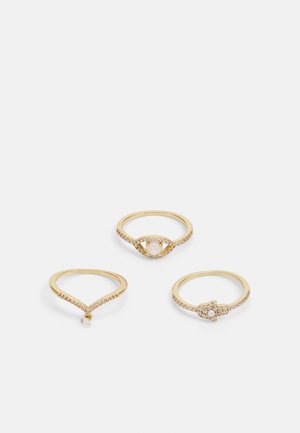 Set aus drei goldenen Ringen. Einer mit einem strukturierten Band und einem kleinen hängenden Stein, einer mit einem ovalen Stein und einem Halo aus Edelsteinen, und einer mit einem kunstvollen Design.