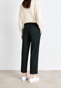 Ciemnozielone, dopasowane spodnie o prostym kroju. Wykonane z gładkiego materiału, z bocznymi kieszeniami i subtelnym detalem logo z tyłu.