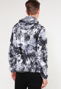 Kurtka z kapturem w teksturowany czarno-biały abstrakcyjny wzór, wykonana z lekkiego materiału. Charakteryzuje się dopasowanym krojem i elastycznymi mankietami.