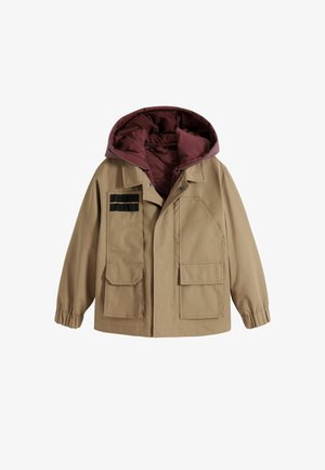 Tan jas met een kastanjebruine capuchon, voorzien van twee zijzakken, een rits en zwarte stoffen strepen op de linkerborst. Duurzaam materiaal, ontspannen pasvorm.