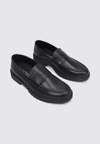 Mocasines de cuero negro con un acabado suave, que presentan un detalle de tira cosida, un perfil bajo y una suela de goma gruesa.