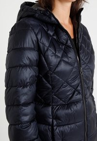 Quilted, navy blue puffer jacket with a hood, featuring a smooth, shiny texture, zipper closure, and angled seams for added detail.