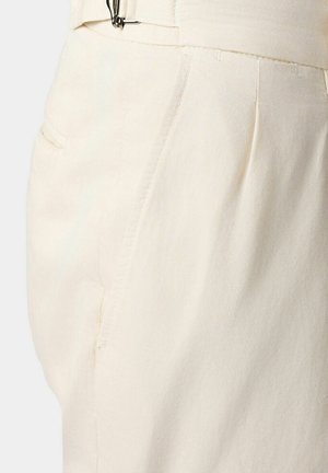 Beige stoffen broek met zijplooien en een zijzak, met een gladde textuur en een op maat gemaakte uitstraling. Een riemlus is zichtbaar.