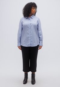 Μπλε και λευκό ριγέ πουκάμισο με κουμπιά και γιακά, συνδυασμένο με μαύρο cropped παντελόνι και μαύρα ankle boots. Λείο ύφασμα και εφαρμοστή γραμμή.