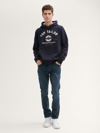 Felpa navy in misto cotone con stampa grafica bianca; tasca frontale; abbinata a jeans blu e sneakers bianche. Taglio casual.