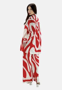 Chemise à manches longues à motifs rouges et blancs associée à un pantalon large assorti ; tissu lisse, coupe ample, et sandales à talons hauts.