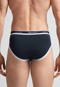 Mörkblå herrbriefs med ett vitt elastiskt midjeband som visar varumärket. Släthett tyg med en åtsittande passform och rundade benöppningar.