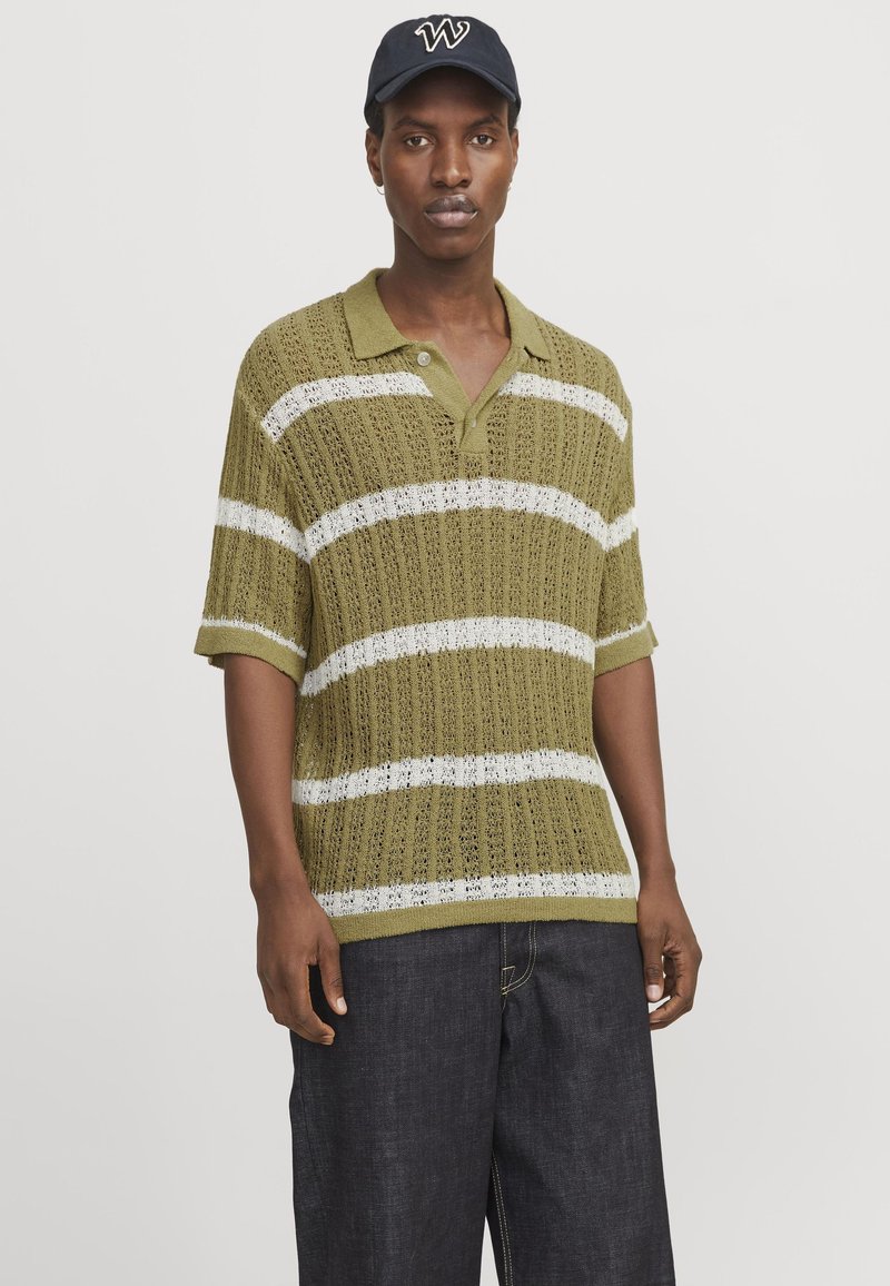 Olivgrön stickad polotröja med vita horisontella ränder, korta ärmar och V-ringning. Matchad med mörk denimbyxor.