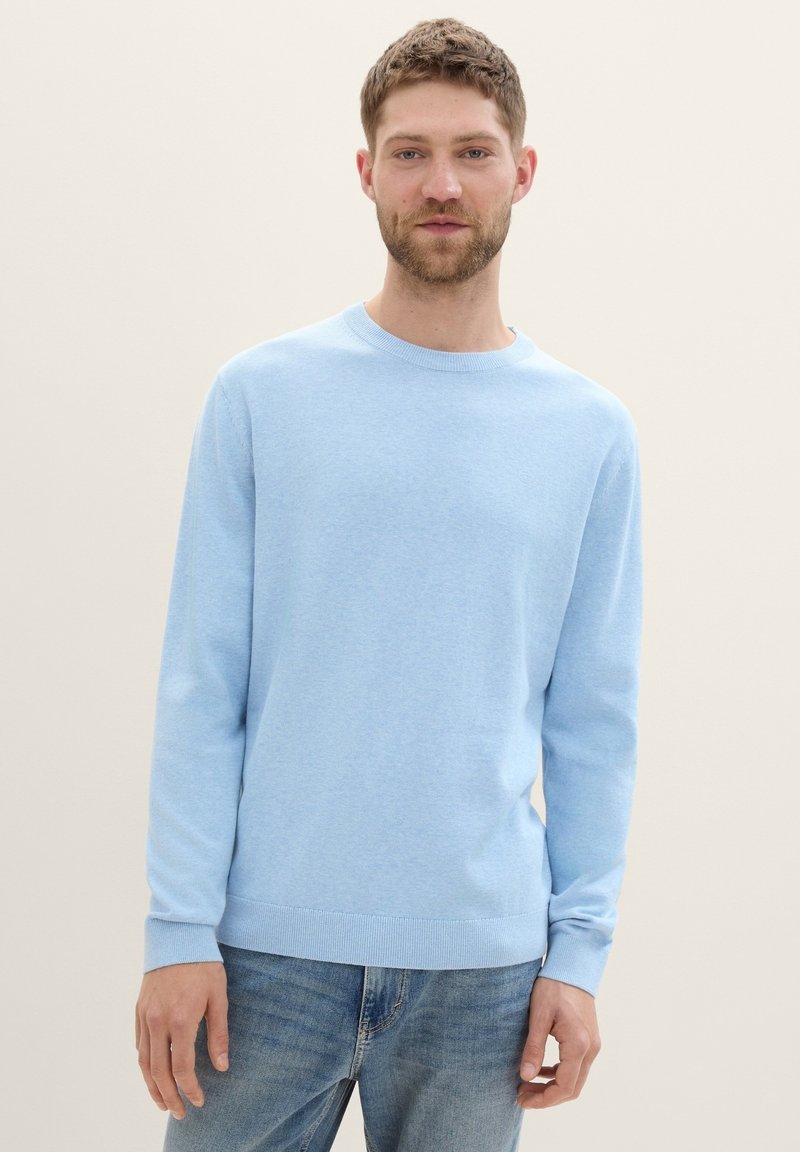 Helle blaue Strickmit Pullover mit langen Ärmeln, rundem Hals und geripptem Saum, kombiniert mit hellblauen Jeans. Weiche Textur und einfaches Design.