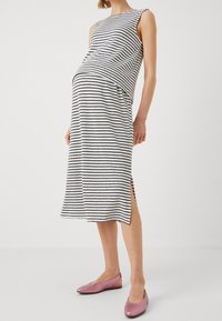 Pruhované těhotenské šaty v černobílé barvě, se volným střihem, bez rukávů, délky ke kalhotkám a bočními rozparky. Růžové baleríny.