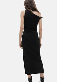 Vestido negro de un solo hombro hecho de una tela suave, diseño ajustado con una abertura a la altura de la rodilla, con un detalle de lazada en el hombro.