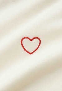 Roter, gestickter Herzumriss auf glattem, cremeweißem Stoff, zentriert im Bild.