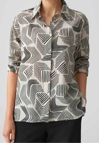 Chemise boutonnée en tissu léger, présentant un motif abstrait noir et blanc de lignes et formes courbes, avec des manches retroussées.