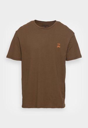 T-shirt marron à manches courtes et col rond avec un petit motif orange et le texte "CORE" sur le côté gauche de la poitrine.