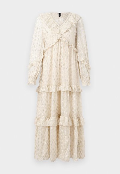 Garšīgs, krēmmelns kleita, kas izgatavota no viegla auduma, ar slāņotu flautu dizainu, V veida kakla izgriezumu un garām piedurknēm ar viļņotiem galiem.