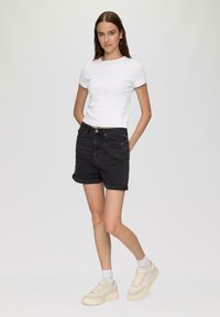 Biała krótko rękawowa koszulka ribbed w połączeniu z czarnymi dżinsowymi szortami. Szorty mają podwinięte mankiety, zestawione z jasnymi platformowymi sneakersami.