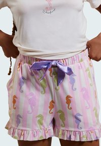 Ljusrosa shorts med dekorativa sjöhästmönster i olika färger, med en volangnert nederkant och en satinlila fluga vid midjan.