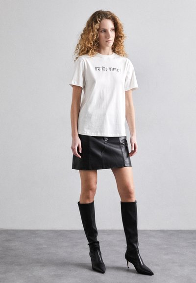 T-shirt en coton blanc avec le texte "reborn?", associé à une mini jupe en cuir noir et des bottes noires à talons aiguilles jusqu'aux genoux. Textures lisses, design épuré.