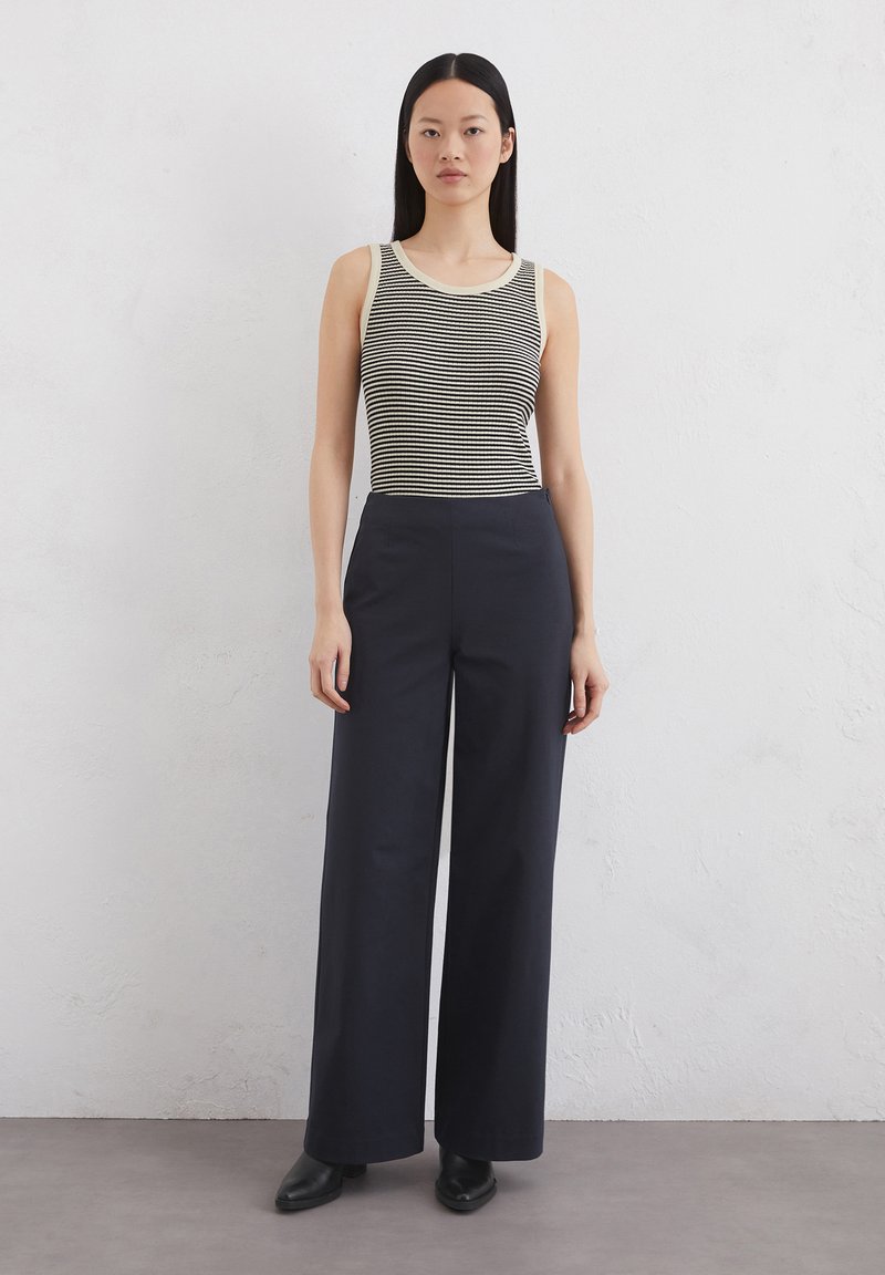 Gestreifter ärmelloser Oberteil mit cremefarbenem Ausschnitt, kombiniert mit hoch taillierten, navyblauen weiten Hosen. Schwarze Stiefeletten runden den Look ab.