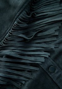 Wildlederjacke in dunkelgrün, mit langen, geschichteten Fransen entlang einer Seite und einem schwarzen Druckknopf-Detail.
