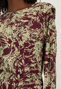 Langemouwen jurk met een abstract patroon in bordeauxrood, groen en crème, gemaakt van een zachte stof met een gathered Taille en gevoerde schouders.