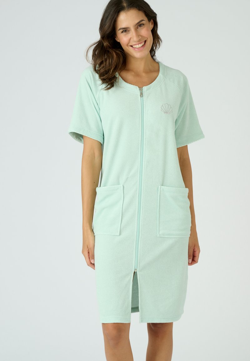 Abito in spugna di colore verde menta chiaro con maniche corte, chiusura con zip completa e due tasche frontali. Presenta un motivo a conchiglia sul petto.