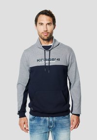 Sudadera con capucha de cuerpo azul marino y mangas a rayas grises. Cuenta con un bolsillo delantero y capucha con cordón. Logo "KGROSHI" en el pecho.