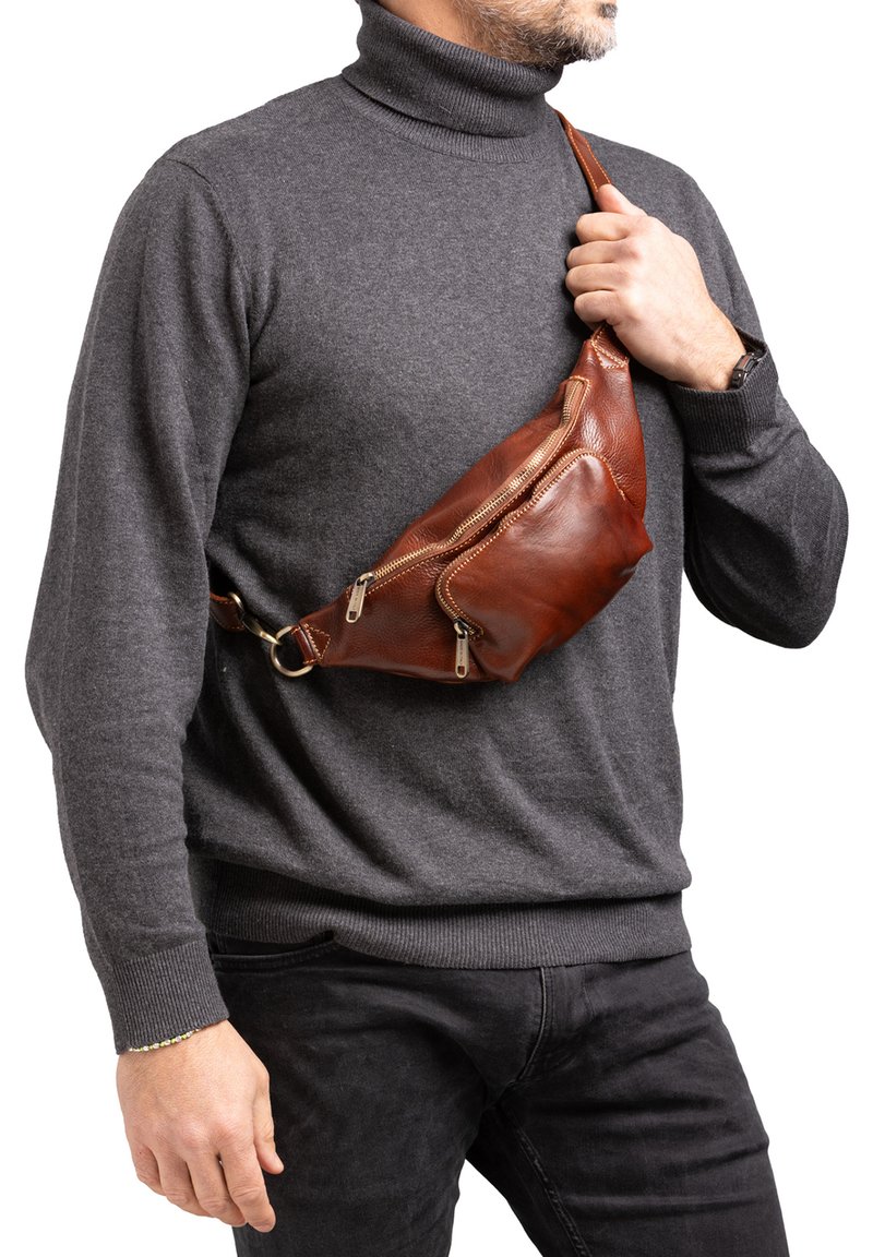 Borsa a tracolla in pelle marrone con due tasche con zip, tracolla regolabile e forma triangolare, indossata sopra un maglione grigio.