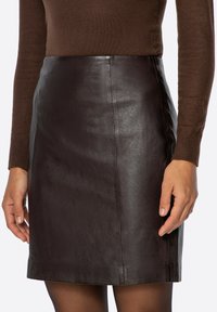 Gonna in pelle marrone con una texture liscia, design aderente e orlo dritto, abbinata a una maglia marrone a maniche lunghe. Dettaglio di cuciture sobrio.