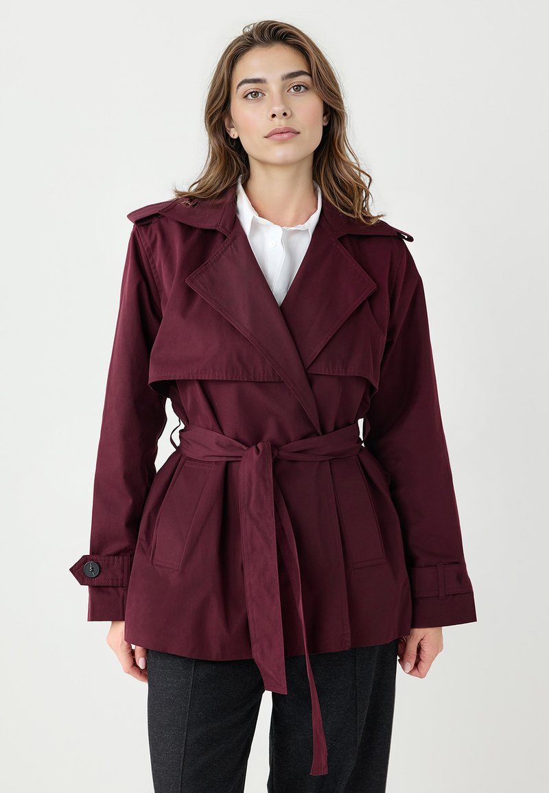 Bordowy płaszcz trencz z paskiem w talii, szerokimi klapami i mankietami na guziki. Wykonany z gładkiej tkaniny o lekko strukturalnym kroju.