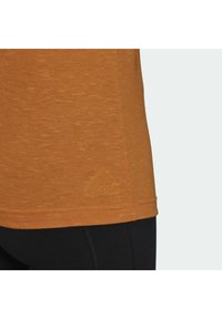 Oranžové sportovní tričko s texturovaným povrchem a malým vyraženým logem Adidas blízko lemování. Kombinováno s černými legínami.