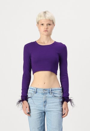 Haut mauve cropped à manches longues avec une texture côtelée et des accents en plumes aux poignets, associé à un jean taille haute bleu clair.