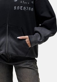 Felpa nera con zip, con testo grafico, polsini a coste e tasche, caratterizzata da un gradiente tonale che va dal grigio scuro al grigio chiaro. Abbinata a jeans scuri.