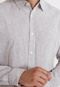 Csíkos inget viselő világosszürke és fehér színben. Klasszikus gallérral, hosszú ujjú és fehér gombokkal rendelkezik. Puha, texturált anyag.
