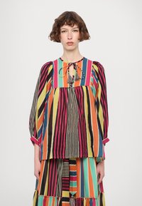Flerfarget stripete bluse med lange ermer, med båndslutt og frynser, laget av et lett materiale.
