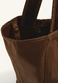 Brown canvas tote bag with sturdy fabric, finished seams, and a metallic snap closure. Thick, brown webbing handles for durability.