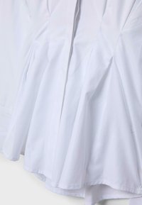 Bela krilo z razširjenim izrezom ali obleka z gubanimi poudarki in šivi vzdolž tkanine, ki ustvarjajo tekočo, voluminozno obliko.