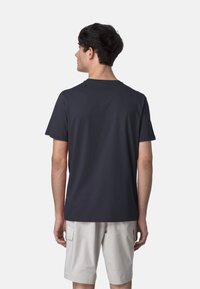 Maglietta a maniche corte blu navy scuro con scollatura rotonda, realizzata in tessuto morbido, vista da dietro. Indossata con pantaloni cargo grigi chiari.