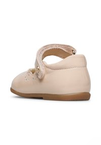 Zapato para bebé de cuero beige claro con punta redondeada, una correa con un acento dorado y detalles cortados en la zona de los dedos. Suela de goma plana.