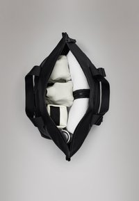Mala de desporto preta com duas alças superiores; o interior contém toalhas brancas enroladas e um item branco, tudo sobre um fundo neutro.