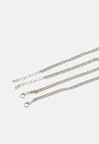 Correntes de metal prateado com um design entrelaçado, com fechos tipo lagosta numa extremidade e elos circulares. Textura lisa com um acabamento brilhante.
