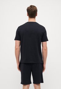 Schwarzes Baumwoll-T-Shirt mit kurzen Ärmeln und Rundhalsausschnitt, kombiniert mit schwarzen Shorts. Einfaches Design ohne sichtbare Logos oder Muster.
