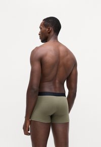 Herrebokser i olivengrønn med svart liv. Tett sitte design vist på en modell bakfra, som fremhever tekstur og form.