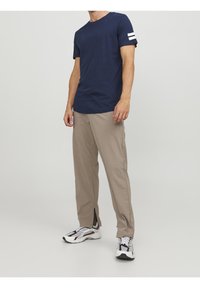 Camiseta de manga corta azul marino con rayas blancas en el brazo izquierdo, combinada con pantalones beige y zapatillas en blanco y negro. Tela suave, ajuste relajado.