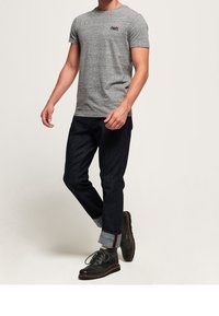 Grå kortärmad t-shirt med en subtil textur och logotyp, kombinerad med mörkblå jeans. Skorna är svarta med en slät yta och snörning.